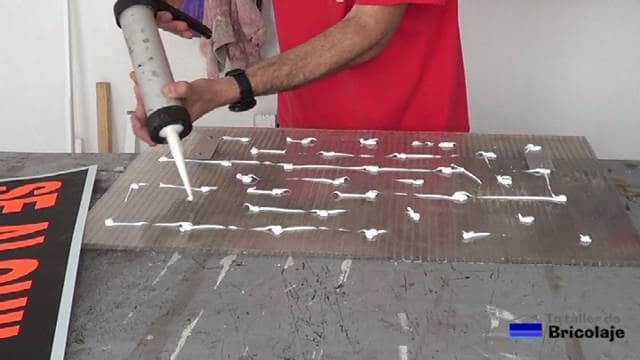 aplicando silicona para pegar el cartel a la plancha de policarbonato